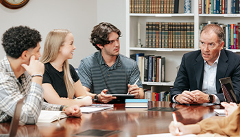 students seated around a large table while listing quietly to a professor