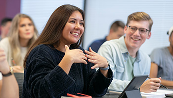 student smiling and talking in a classroom with students seated behind her