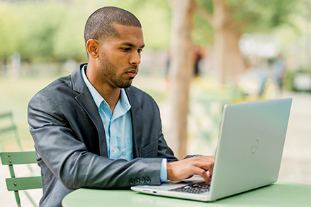 college student typing on computer while sitting outside in downtown Dallas